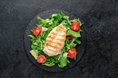 grilled chicken breast with vegetables  on a black plate. top view. 