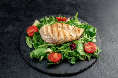 grilled chicken breast with vegetables  on a black plate. top view. 
