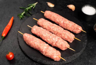 raw meat skewers with spices and herbs on a black background