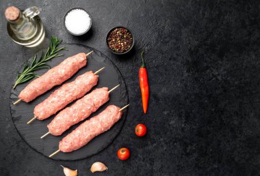 raw meat skewers with spices and herbs on a black background