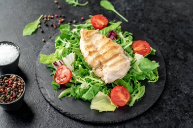 grilled chicken breast with vegetables  on a black plate. top view. 