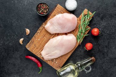 Baharatlı çiğ tavuk göğsü ve siyah arka planda otlar.