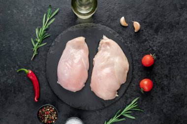 Baharatlı çiğ tavuk göğsü ve siyah arka planda otlar.