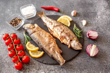 Siyah taş arka planda sebzeli ve baharatlı ızgara alabalık balığı.