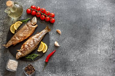 Siyah taş arka planda sebzeli ve baharatlı ızgara alabalık balığı.