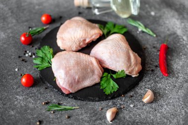 Biberiyeli çiğ tavuk budu ve siyah arka planda baharatlar.