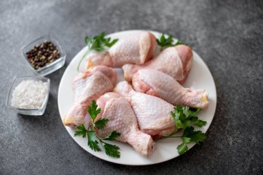 Baharatlı çiğ tavuk budu ve siyah arka planda otlar.