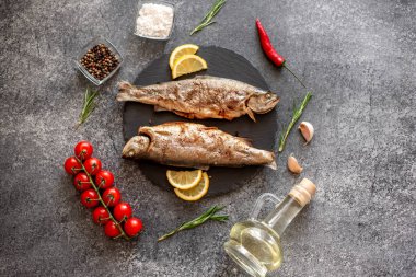 Siyah taşlı arka planda sebzeli ve baharatlı ızgara balık.