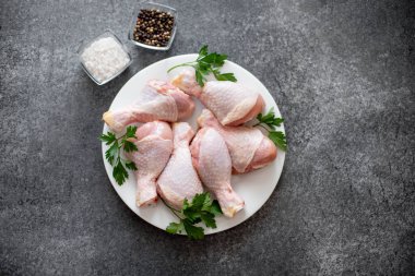 Baharatlı çiğ tavuk budu ve siyah arka planda otlar.