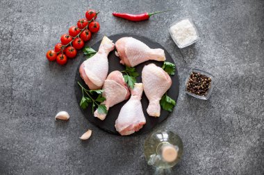 Baharatlı çiğ tavuk budu ve siyah arka planda otlar.