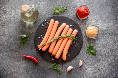 Biberiyeli çiğ sosisler ve gri arka planda bitkiler. 