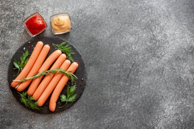 Biberiyeli çiğ sosisler ve gri arka planda bitkiler. 