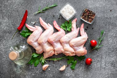 Baharatlı çiğ tavuk kanatları, otlar ve sebzeler siyah taş arka planda