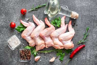 Baharatlı çiğ tavuk kanatları, otlar ve sebzeler siyah taş arka planda