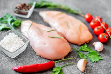 Baharatlı çiğ tavuk göğsü ve taş tahtada otlar.