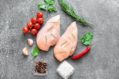 Baharatlı çiğ tavuk göğsü ve taş tahtada otlar.