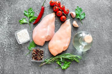 Baharatlı çiğ tavuk göğsü ve taş tahtada otlar.
