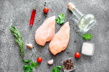Baharatlı çiğ tavuk göğsü ve taş tahtada otlar.