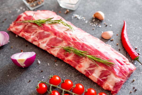 raw pork ribs with rosemary and spices on grey stone background