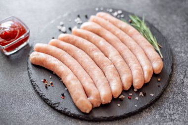 Biberiyeli çiğ et sosisleri ve gri arka planda baharatlar.