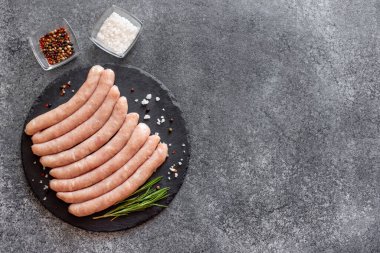 Biberiyeli çiğ et sosisleri ve gri arka planda baharatlar.