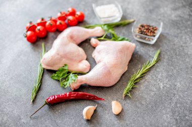 Çiğ tavuk budu, bitkiler ve baharatlar gri taş arka planda. 