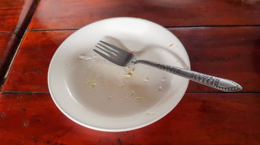 Pastayı yemekten arta kalan tabağa bir parça pasta yapışmış ve daha yıkanmadan tabağa bir çatal yerleştirilmiş..