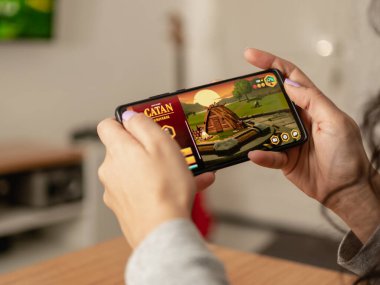 Woman holding smartphone while playing Catan with the mobile App. Close up caption, Selective focus. July 13, 2022. Rio Negro, Argentina