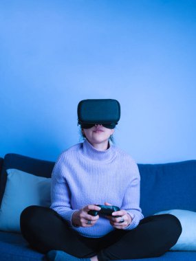 Young woman concentrated on playing video games with VR glasses for smartphone at home. Vertical shot