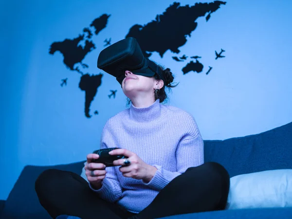 Brunette young woman playing with VR gaming set for smartphone while sitting on the couch at home