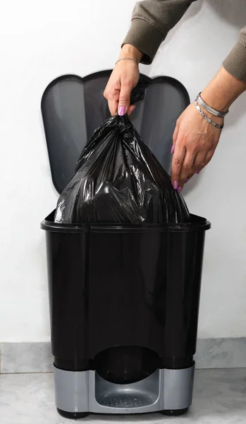 Woman hand taking bag from garbage bin at home. Close up caption. Vertical