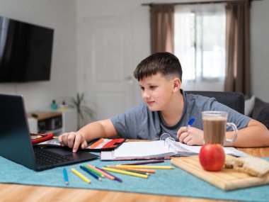 Caucasian schoolboy doing homework with his laptop and a snack. E-learning concept