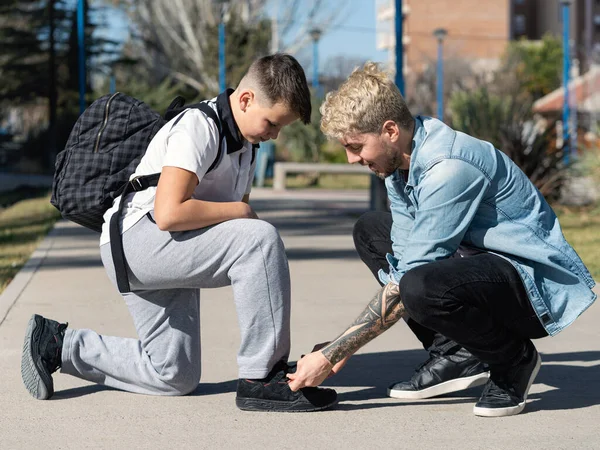 Father helping his son to tie his shoelaces in the street, on their way to school