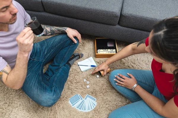 Couple rolling dices and drinking coffee while sitting on the carpet. Top view