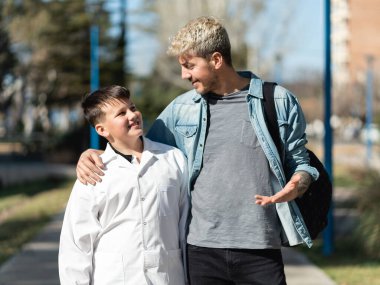 Caucasian father and son talking while walking to school in Argentina. Kid is wearing a white coat (guardapolvo) typical for public schools in Argentina