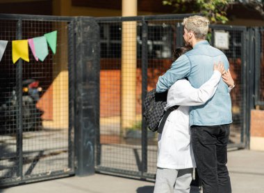 Baba, Arjantin 'deki devlet okuluna girmeden önce oğluna sarılıyor. Oğlan beyaz önlük giyiyor (guardapolvo), Arjantin 'deki devlet okulları için tipik bir kıyafet.
