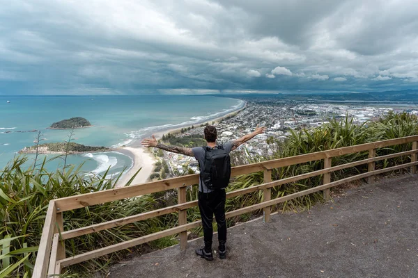 Man with open arms at Mount Maunganui lookout on a beautiful day. North Island, New Zealand