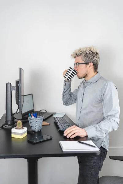 Businessman in standing desk working and drinking coffee. Comfort at work concept. Vertical photo
