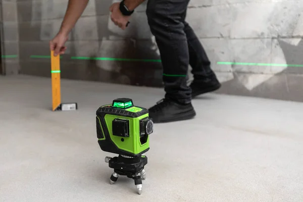 Робочий інспектор перевіряє рівень підлоги за допомогою вимірювача рівня лазера, який проектує зелені лінії на цементних стінах на будівельному майданчику . Стокове Фото