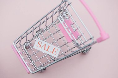 Pembe arka planda satılık sözcüğü olan küçük bir alışveriş arabası.