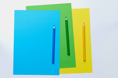 Yeşil, mavi ve sarı renkli üç renkli kalem kopya alanı ile eşleşen kağıdın üzerinde yatar.