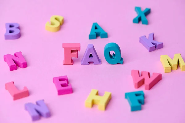 Wooden letters with the word FAQ which means frequently asked questions on pink background with colorful letters around. Collection of frequently asked questions on any topic and answers to them