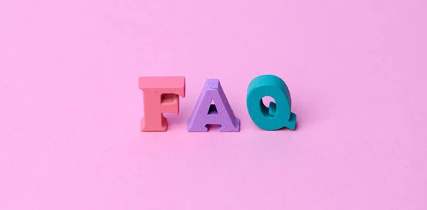 Wooden letters with the word FAQ which means frequently asked questions on pink background. Collection of frequently asked questions on any topic and answers to them