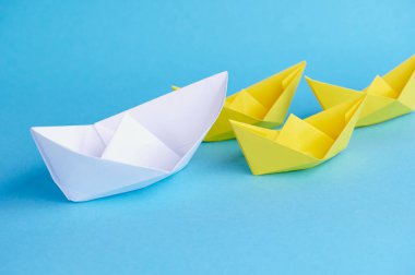 A big white paper boat leads small yellow paper boats as a team. Concept for teamwork, cooperation, leadership as well as partnership.