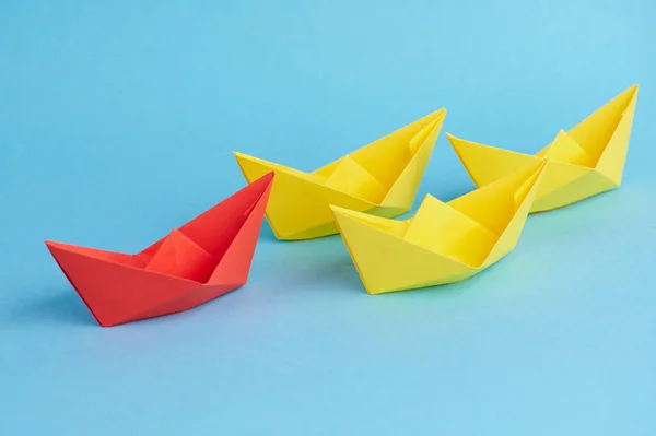 A red paper boat leads small yellow paper boats as a team. Concept for teamwork, cooperation, leadership as well as partnership.