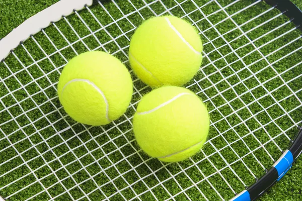 Three tennis balls lie on a tennis racket strings.