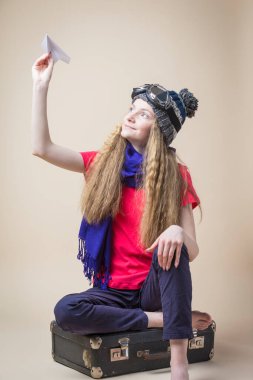 Uçan Dişli Genç Kız ve Sıcak Şapka Ören Origami Kağıt Uçağı Eski Bavul 'un üzerinde otururken Bej Arkaplan Üzerinde Kalkıyor. Dikey Resim Kompozisyonu