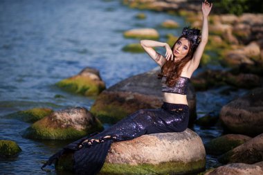 Asyalı Denizkızı Kayaların Üzerinde Okyanus Kıyısı Poz Verirken Deniz Kabuğu Takılı Siyah Parlak Kuyruklu Şahane Deniz Kraliçesi rolüyle seksi vücutlu tacını takıyor. Yatay Yönlendirme