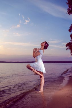 Beyaz elbiseli Japon bale dansçısıyla dans etme tutkusu ve okyanus dalgalarında duran gümüş taç ve deniz manzaralı günbatımına karşı kaldırılmış el ile bale Pas gösterisi.