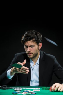Kumarhane Kavramları. Poker masasında fiş ve kartlarla kağıt oynayan yakışıklı, beyaz tenli, genç bir poker oyuncusu. Dikey Resim